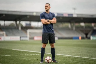 Défenseur central du PSG en position d'autorité sur le terrain d'entraînement, bras croisés, regard concentré, symbolisant la solidité défensive en 2026