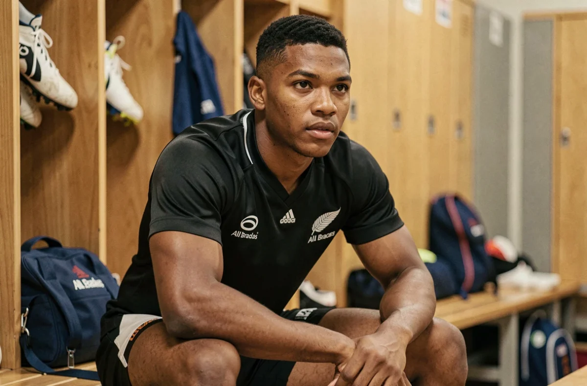 Jeune joueur des All Blacks assis dans les vestiaires en maillot noir avant un match, ambiance documentaire